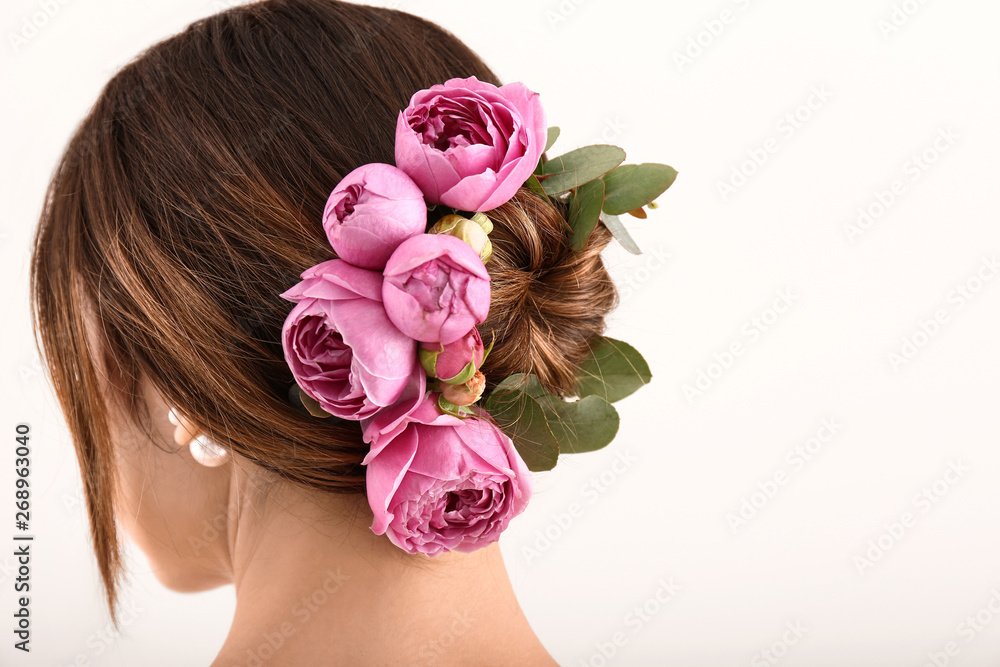 Young woman with beautiful flowers in her hair on light background, back view