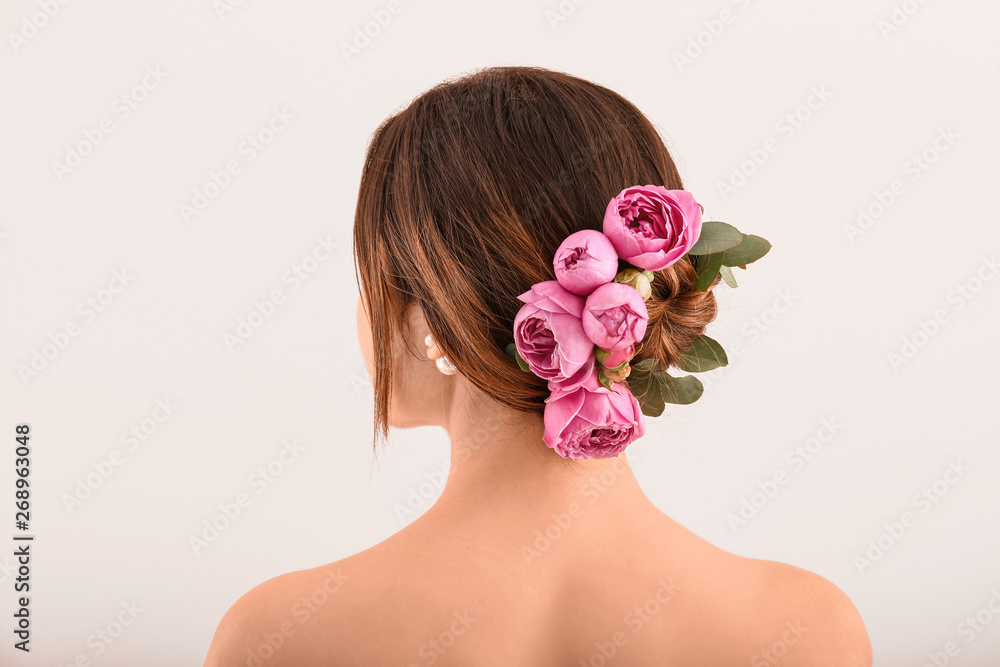 Young woman with beautiful flowers in her hair on light background, back view