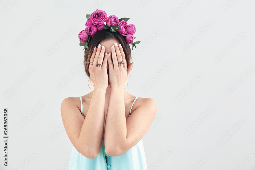 Young woman with beautiful flowers on her head on light background