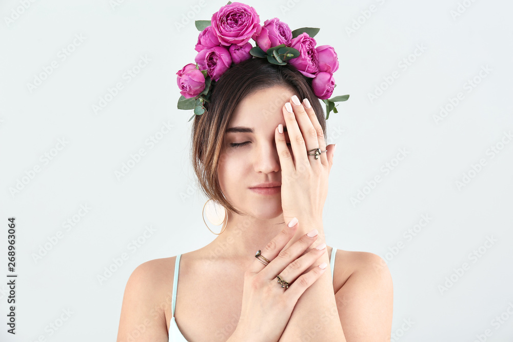 Young woman with beautiful flowers on her head on light background