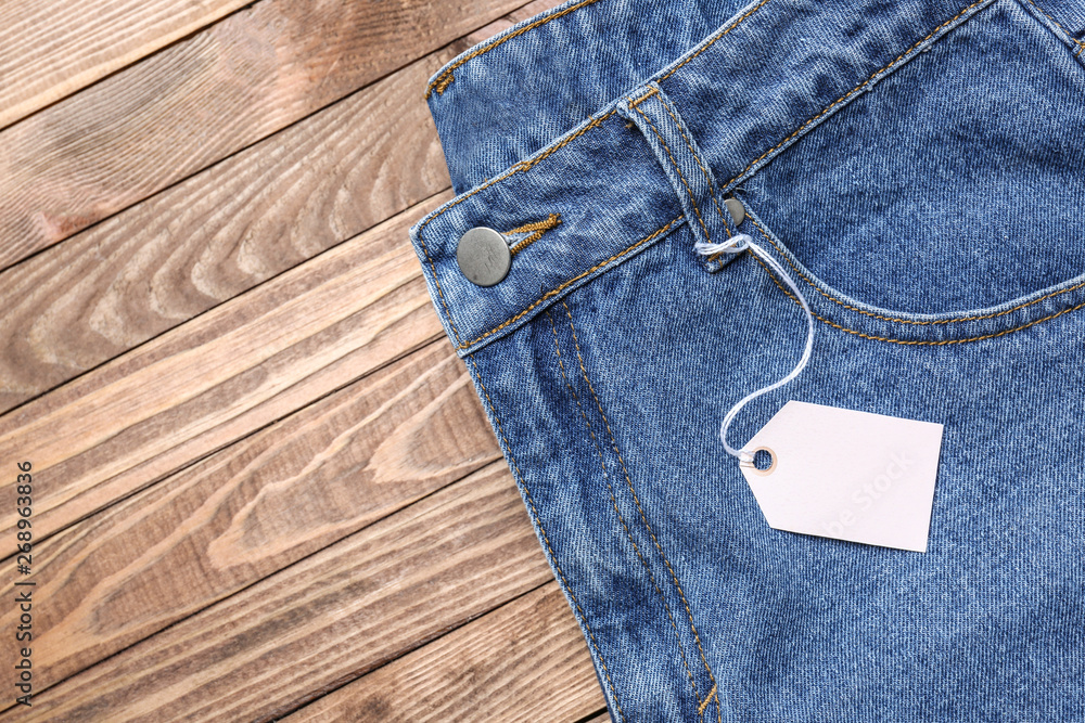 Stylish jeans with tag on wooden background