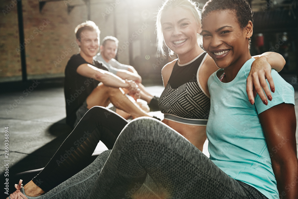 Two smiling women sitting in a gym after working out