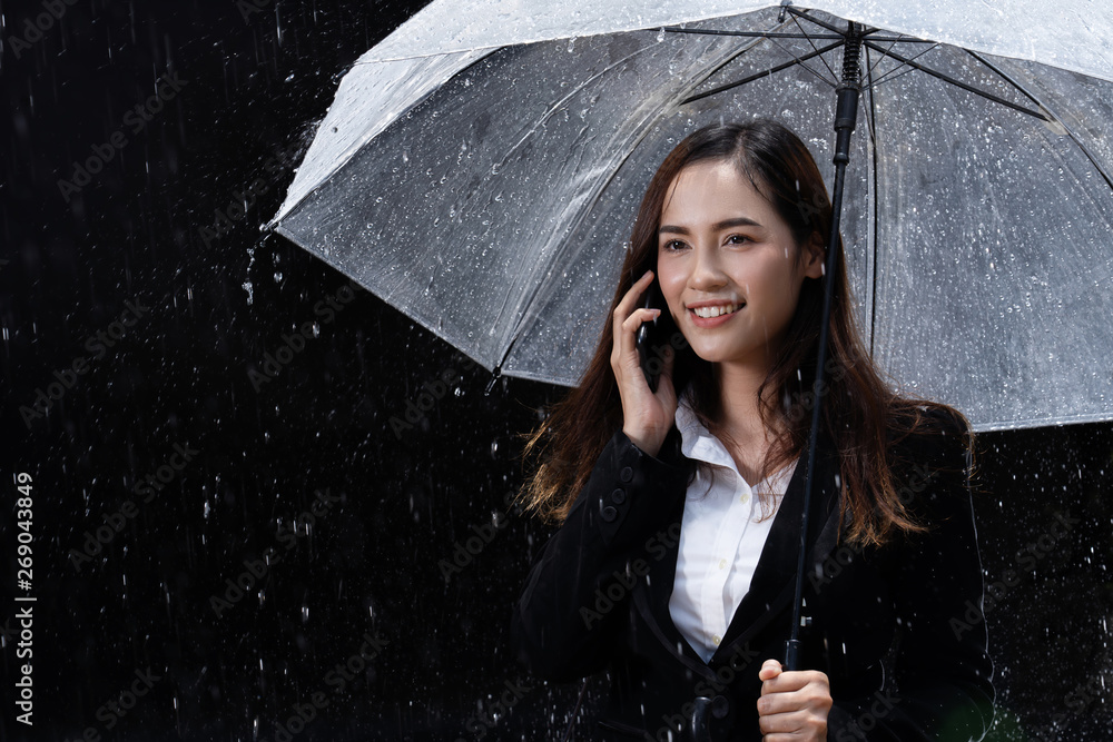 亚洲女子正在打伞，雨正在下。她正在打电话