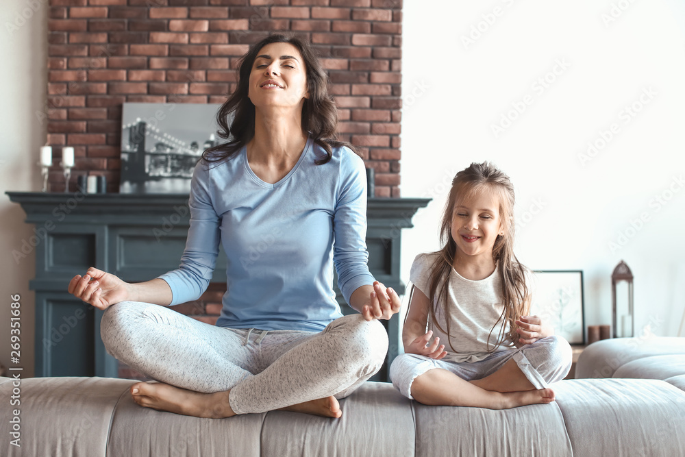 Mother with little daughter meditating at home