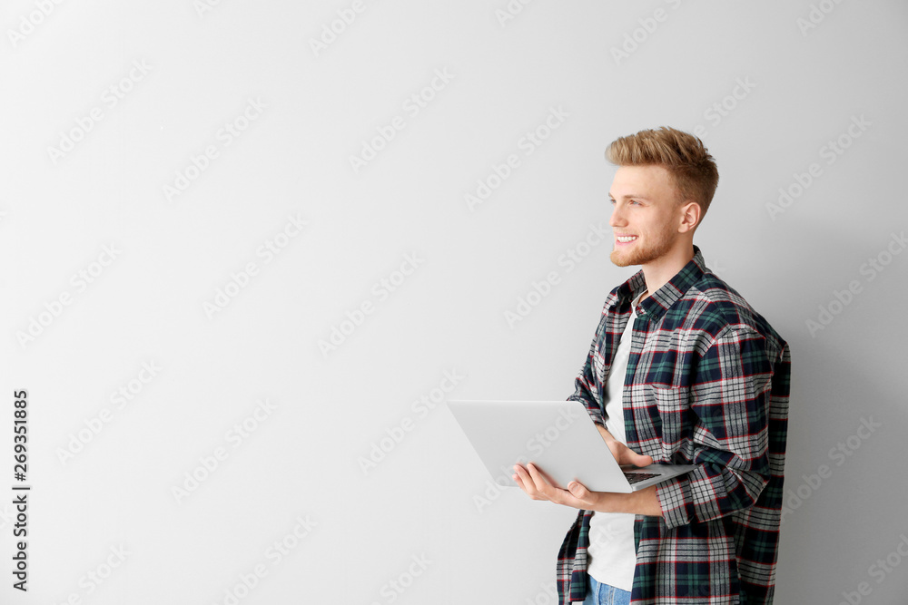 Handsome young man with laptop on light background