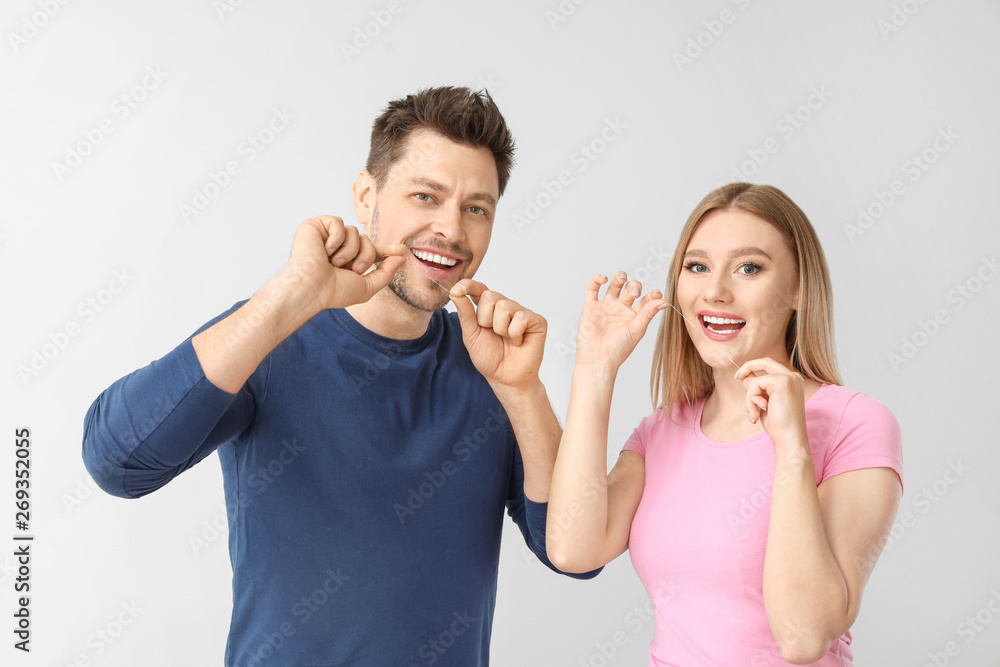 Man and woman flossing teeth on light background