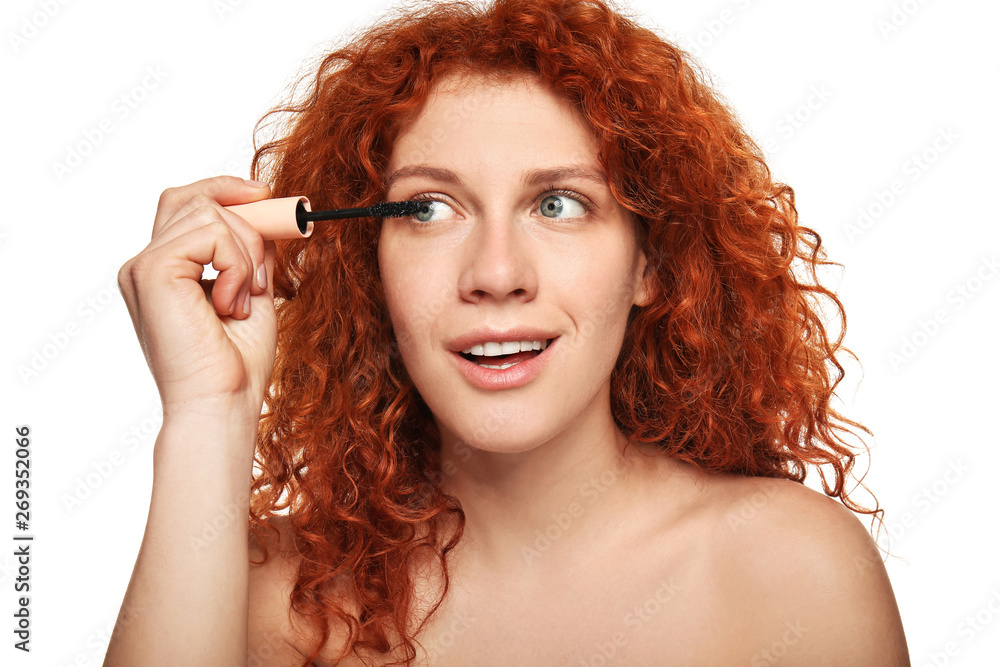 Beautiful young woman applying mascara against white background