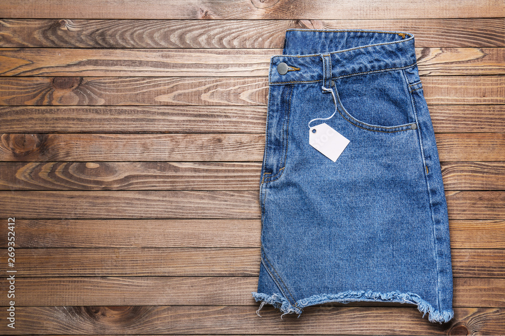 Stylish jeans skirt with tag on wooden background