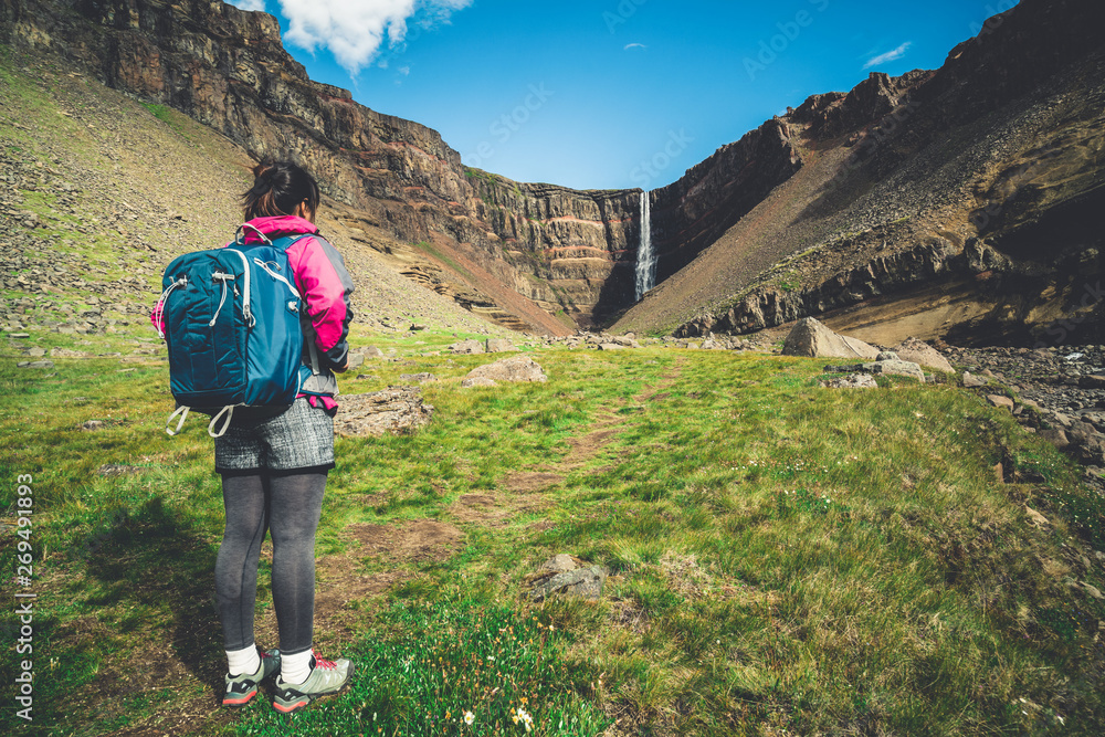 Woman traveler trekking in Icelandic summer landscape at the Hengifoss waterfall in Iceland. The wat