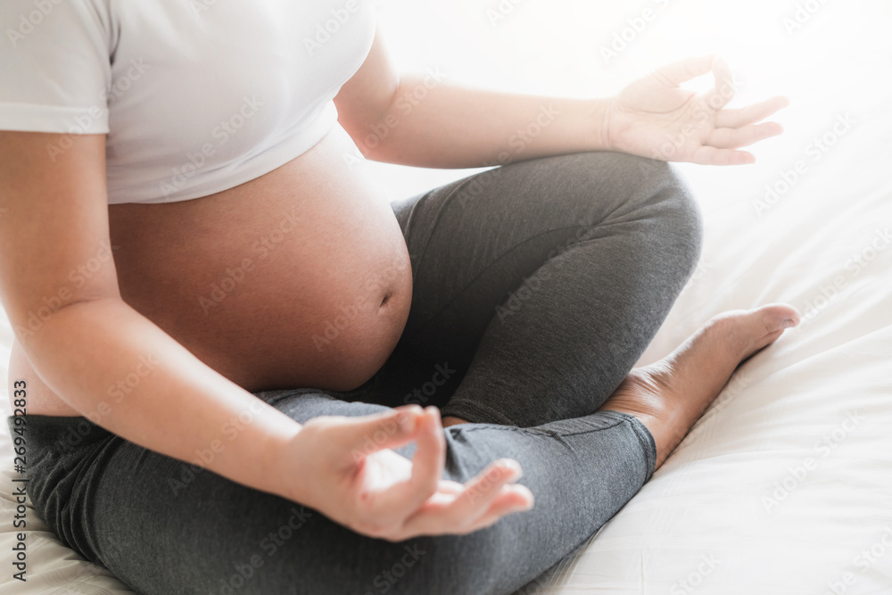 Pregnant woman doing yoga exercise on bed in bedroom at home while taking care of her child. The hap