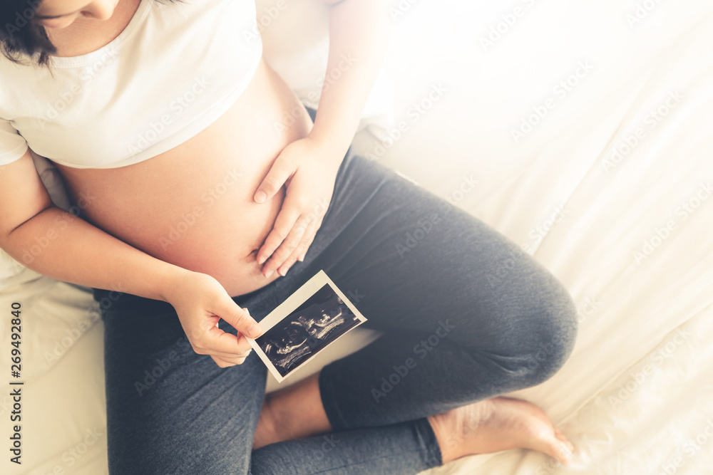 Pregnant woman feeling happy at home while taking care of her child. The young expecting mother hold