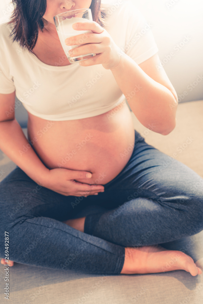 Happy pregnant woman drinks milk in glass at home while taking care of her child. The young expectin