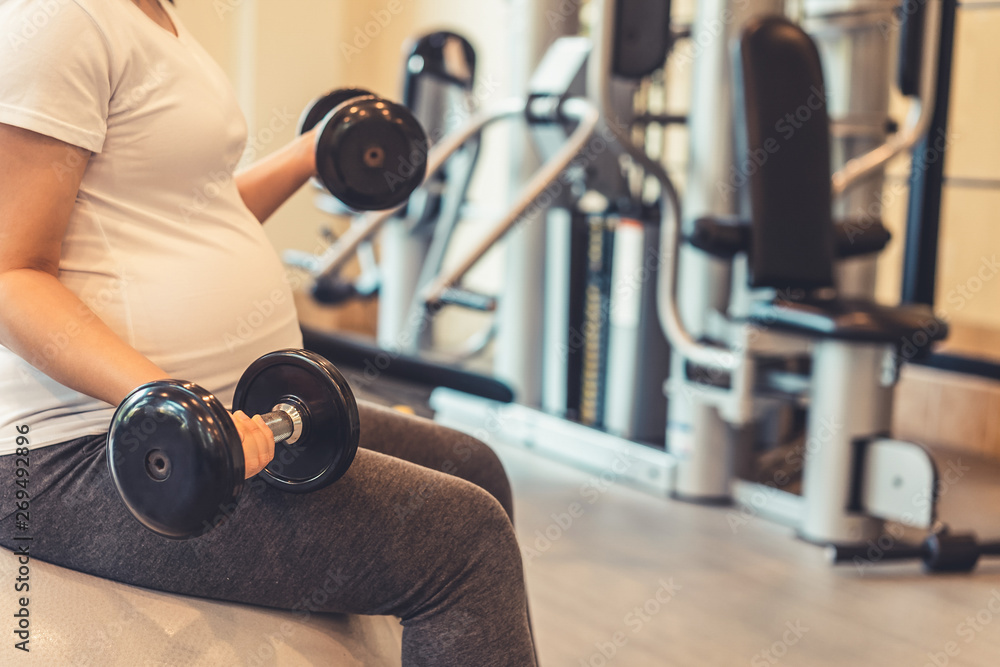 Active pregnant woman exercise in fitness center at yoga room. The young expecting mother holding ba