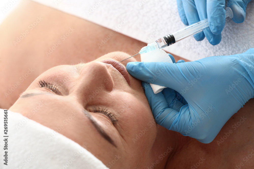 Mature woman receiving filler injection in beauty salon, closeup