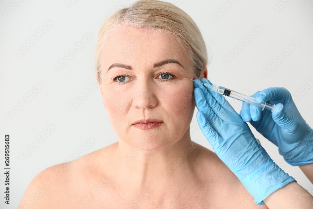 Mature woman receiving injection in face on light background