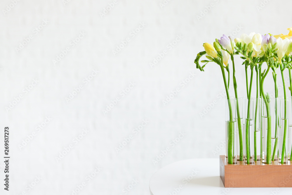 Beautiful freesia flowers on table against light background