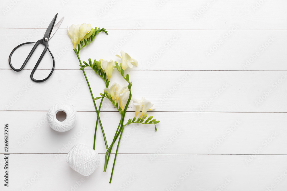 Beautiful freesia flowers, scissors and thread on white wooden table