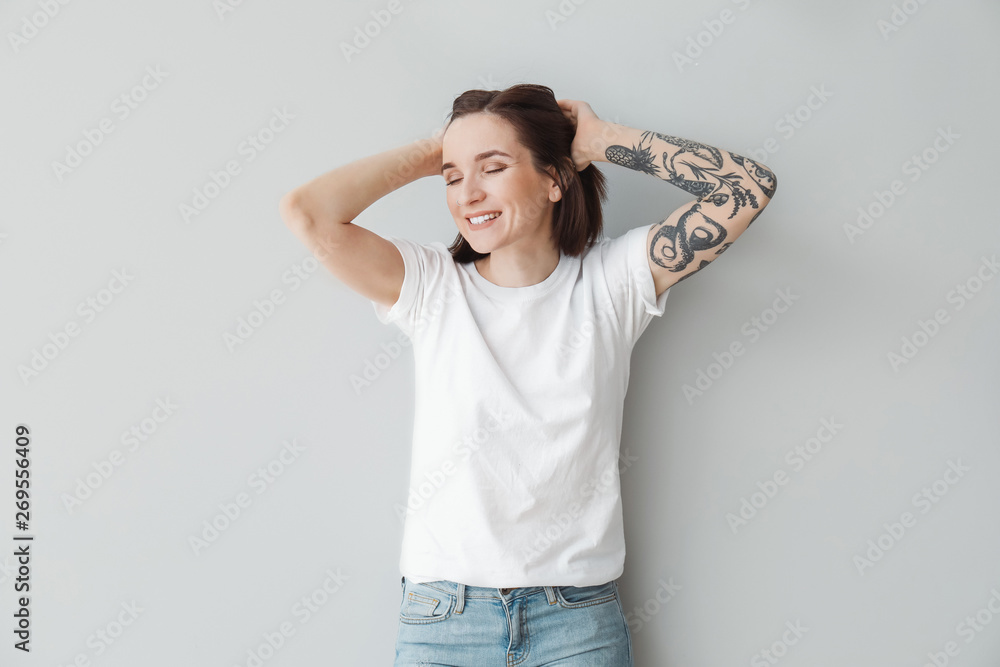 Stylish tattooed woman on light background