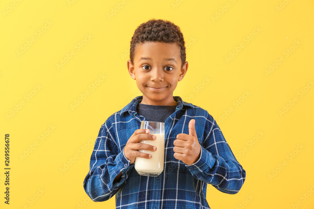 Cute African-American boy with glass of milk showing thumb-up on color background