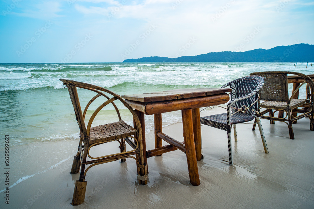 Bamboo table and wooden chairs in empty cafe next to sea water in tropical beach. Close up. Island K