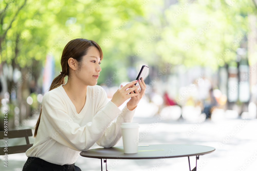 オープンカフェでスマートフォンを使う女性