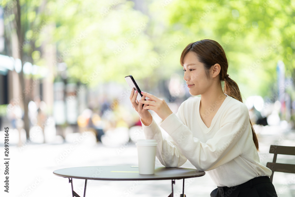 オープンカフェでスマートフォンを使う女性