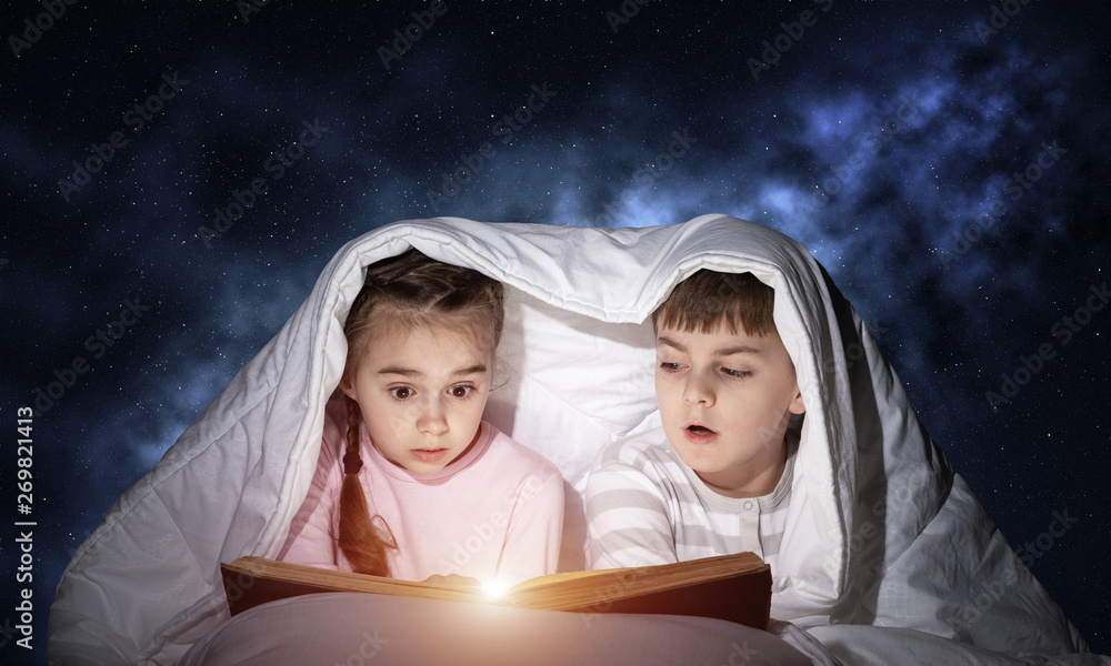 Children reading scary stories in bed