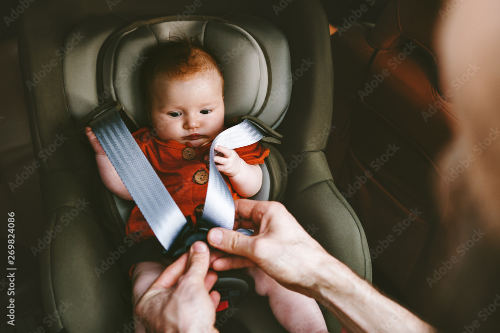 Baby sitting in safety car seat and father fastens belt happy family lifestyle vacation road trip ch