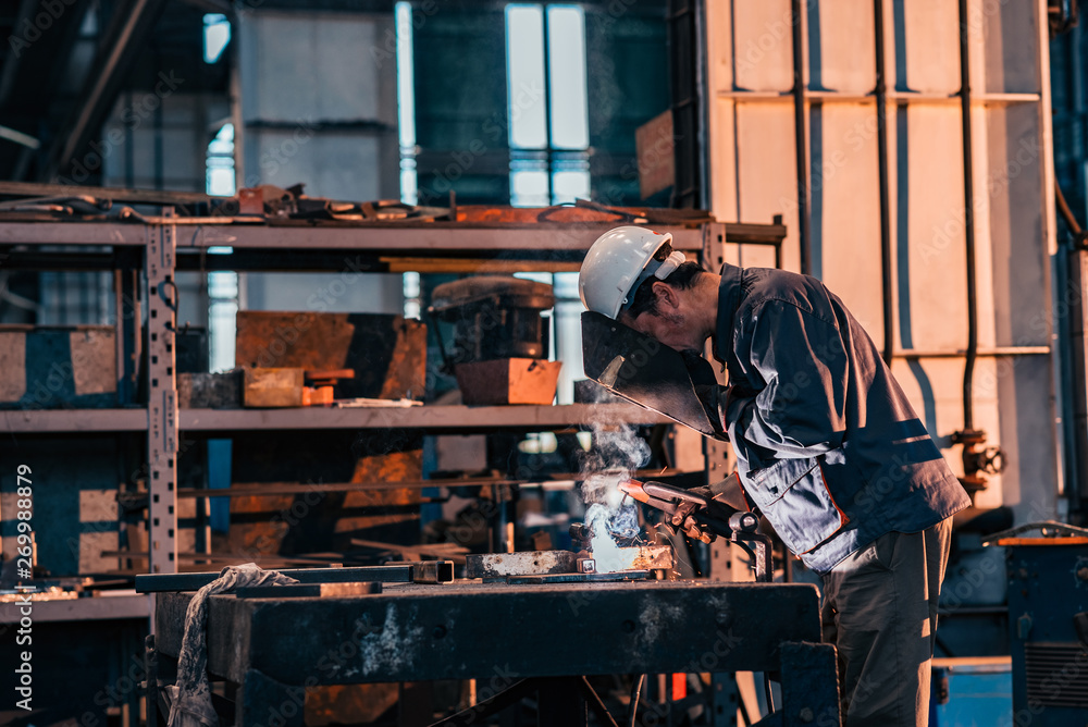 Side view of factory worker welding in metal industry workshop.