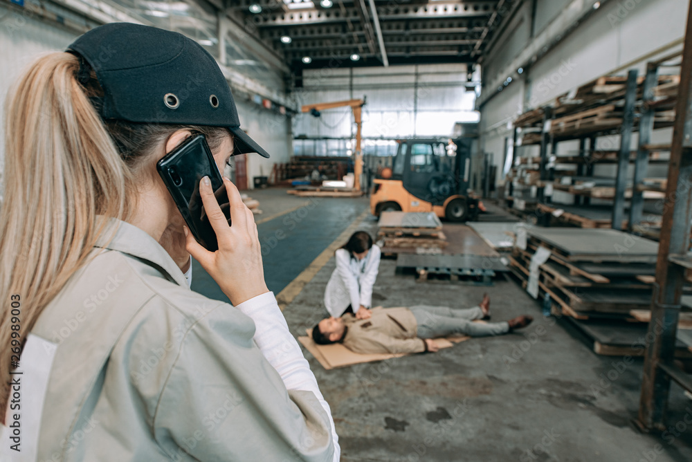 Female factory worker calling ambulance while doctor giving CPR to a worker.