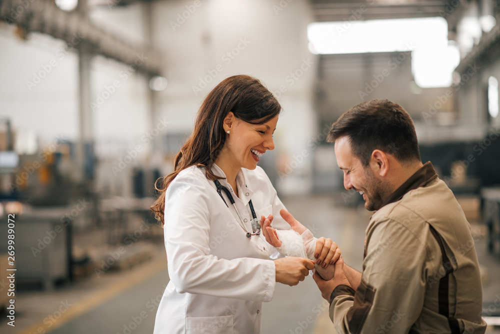 Smiling female doctor with injured worker in the industrial building.