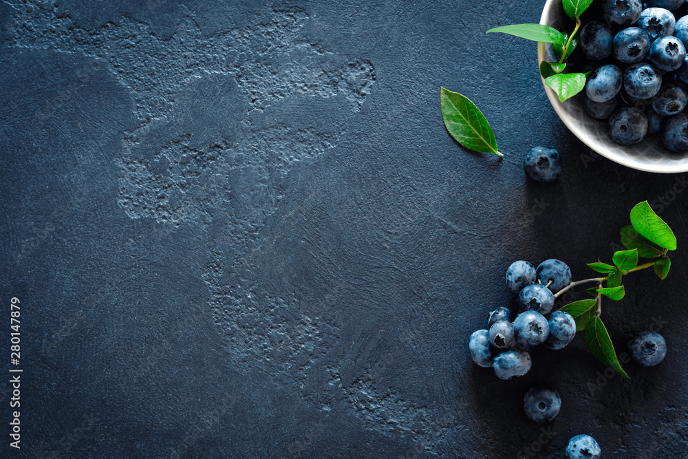 Blueberries with leaves on black background, top view