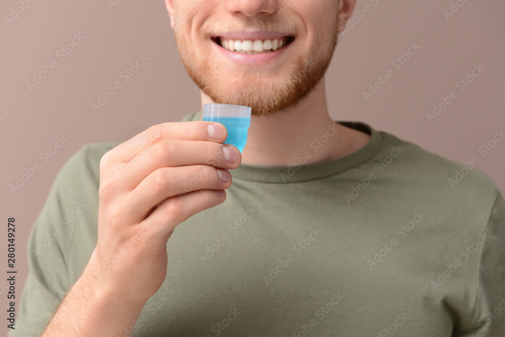 Young man with cup of mouthwash on color background