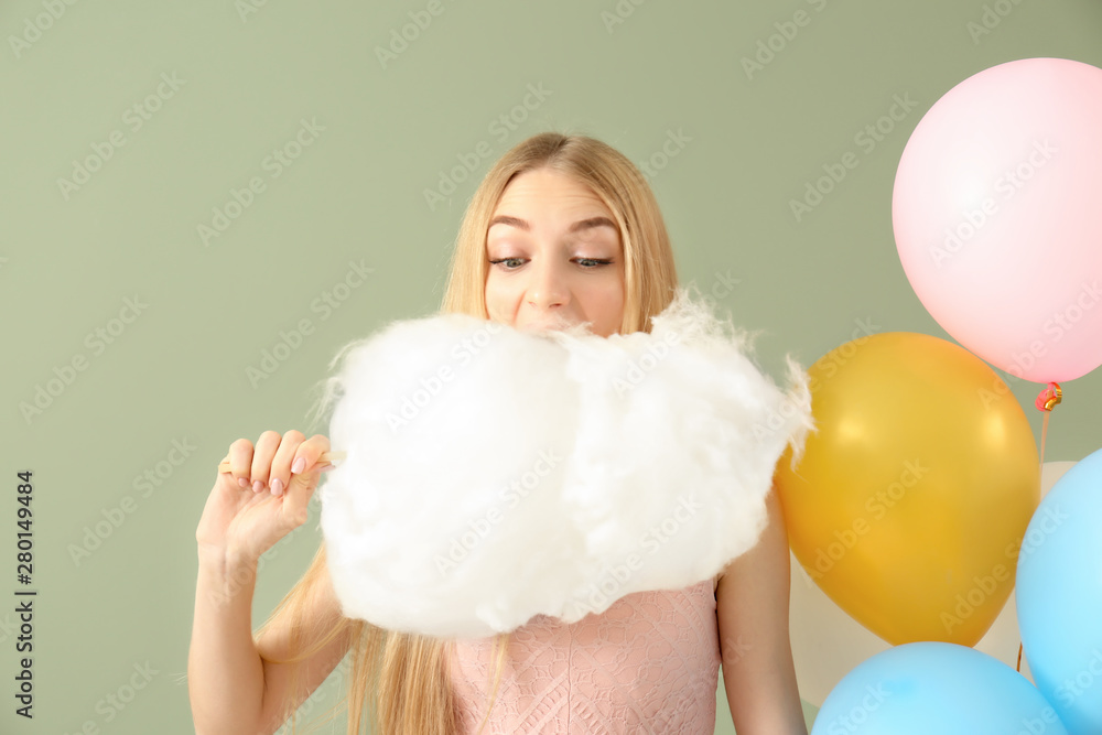 Beautiful woman with cotton candy and air balloons on color background