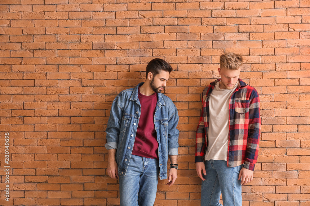 Fashionable young men near brick wall