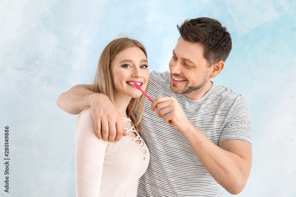 Man cleaning teeth of his wife on light background