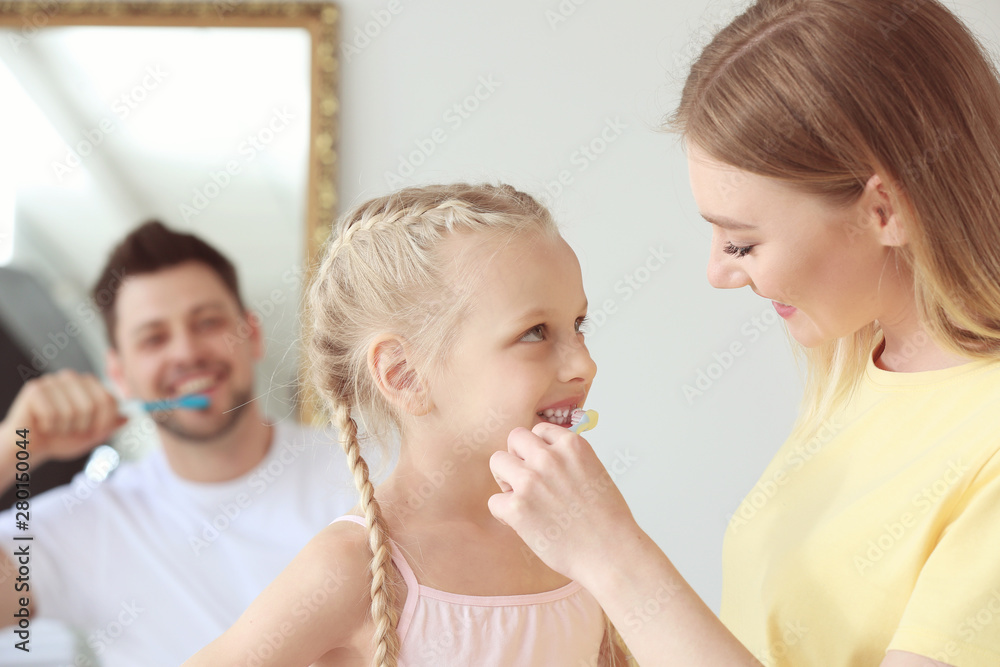 Mother teaching little girl to clean teeth at home