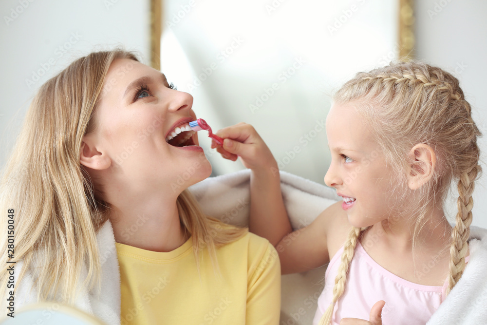 Little girl cleaning teeth of her mother at home