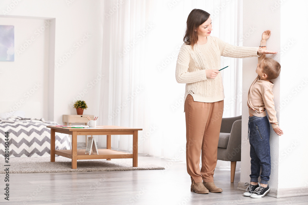 Woman measuring height of her little son near wall