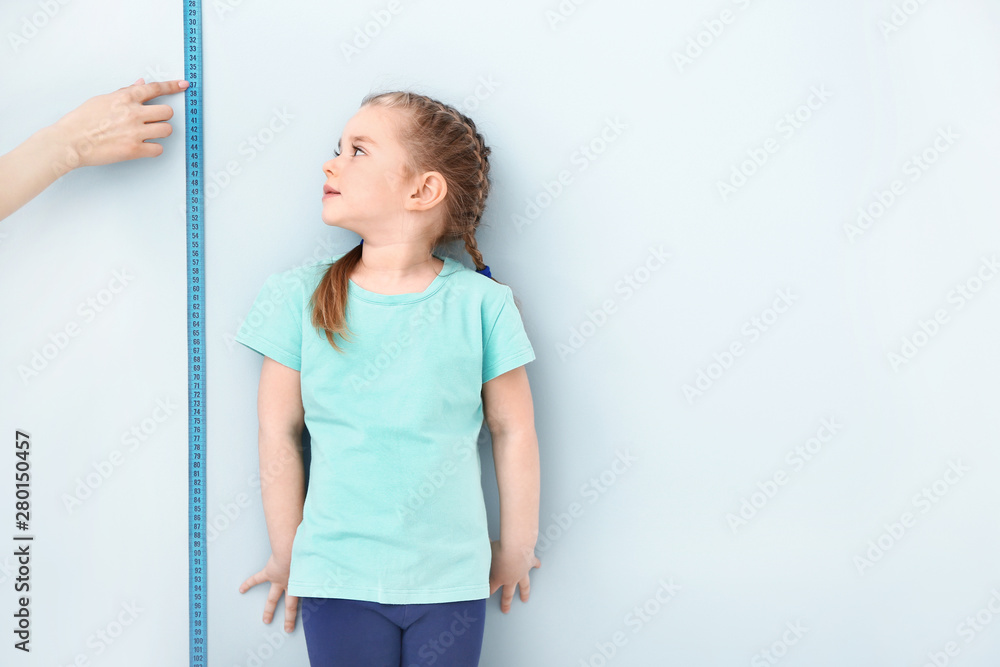 Mother measuring height of little girl near wall