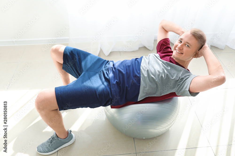 Young man doing exercise with fitball at home