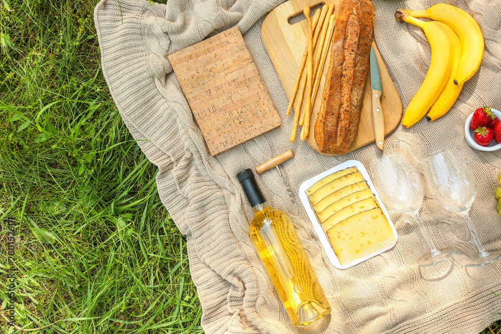 Tasty food and drink for romantic picnic on plaid in park