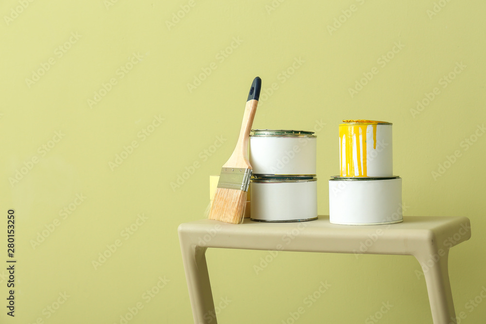 Cans of paint with brush on step ladder against color background