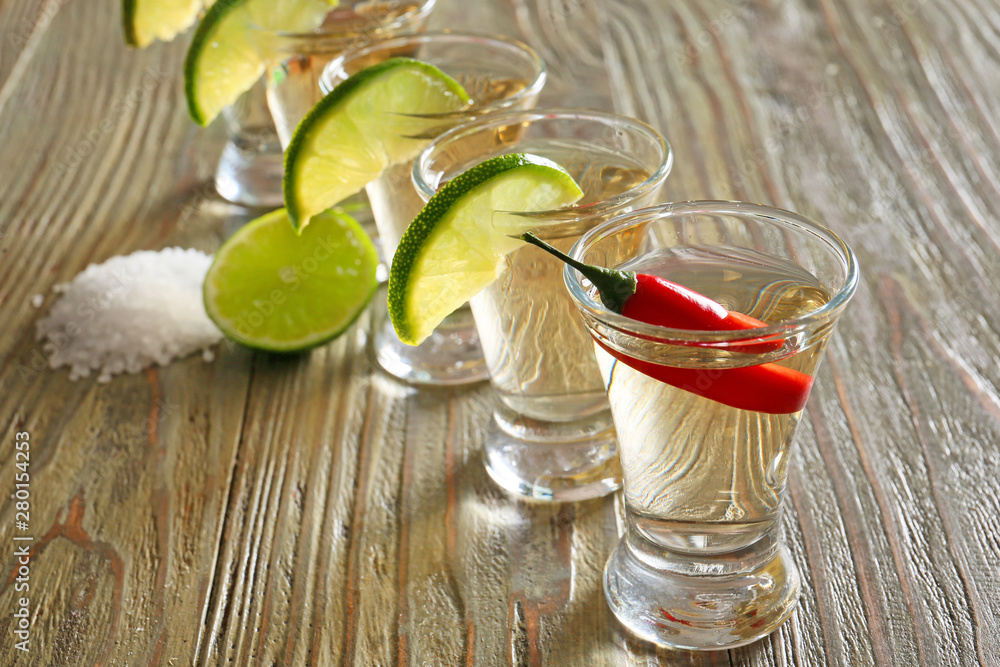 Shots of tasty tequila with lime, salt and chili pepper on wooden table