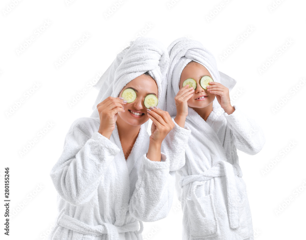 Mother and her little daughter in bathrobes and with cucumber slices on white background