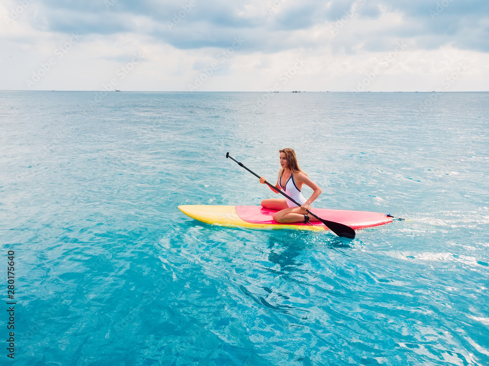 Aerial view of woman on stand up paddle board in blue ocean.