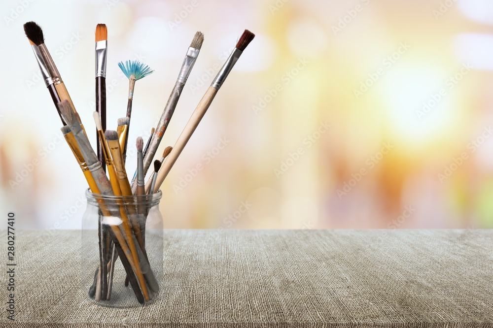 Brushes in a glass jar on the table and white wall