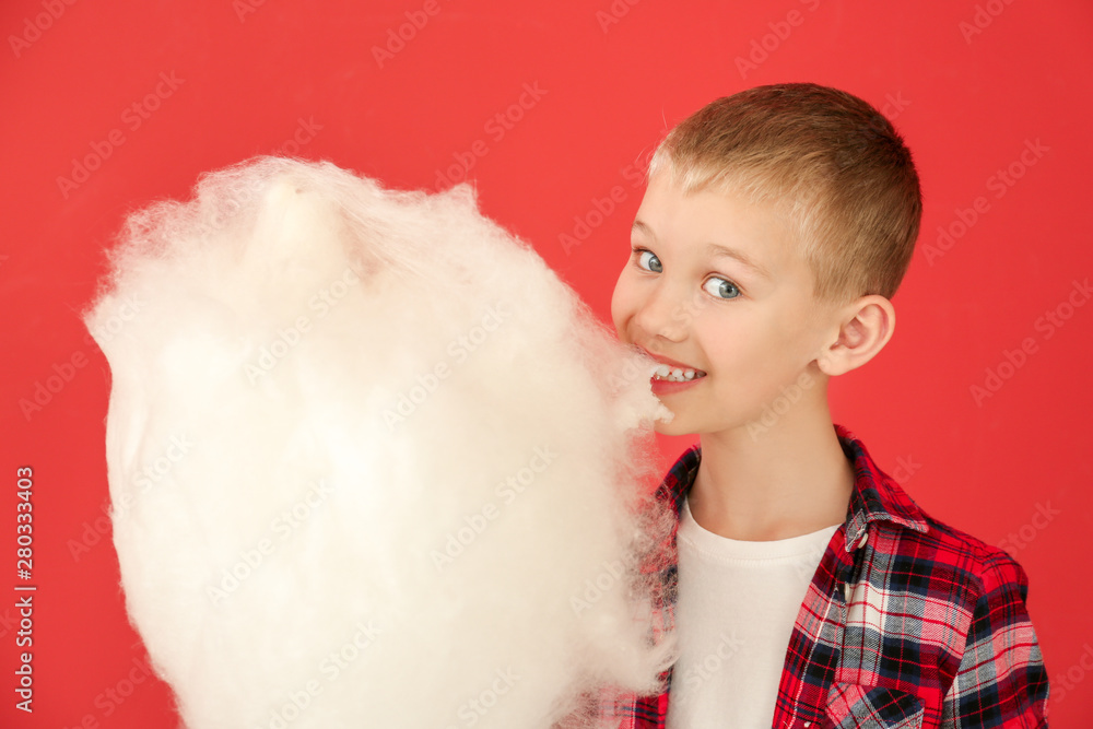 Cute little boy with cotton candy on color background