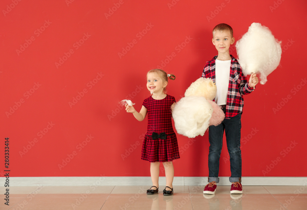 Cute little children with cotton candy against color wall