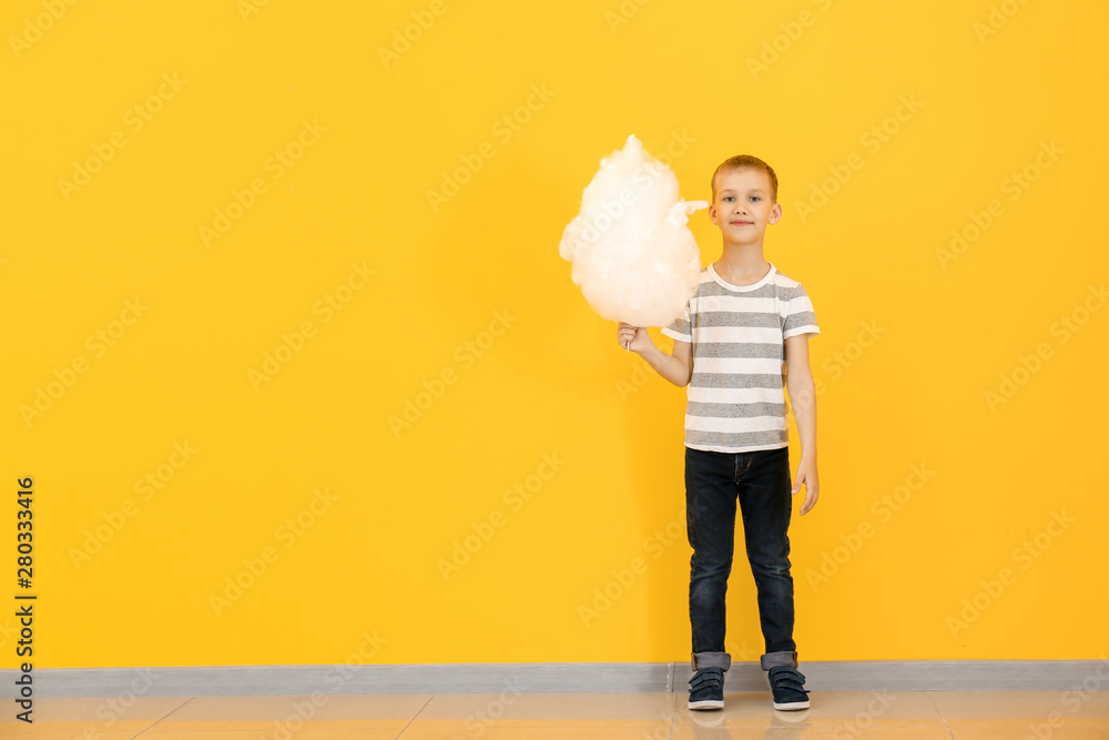 Cute little boy with cotton candy against color wall